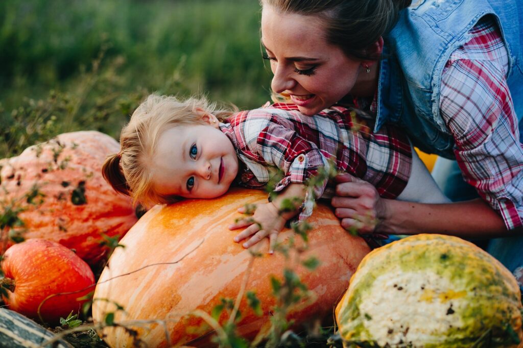 toddler girl resting on a pumpkin being hugged by her mom