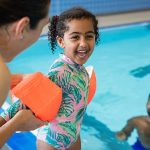Summer Safety: mother putting arm floaties on a child while dad waits in the pool
