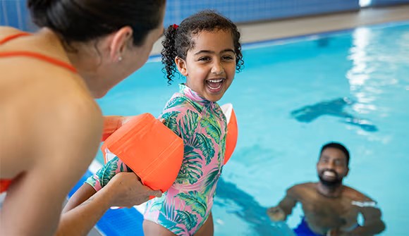 Summer safety: mother putting pool floaties on a child while dad waits in the pool